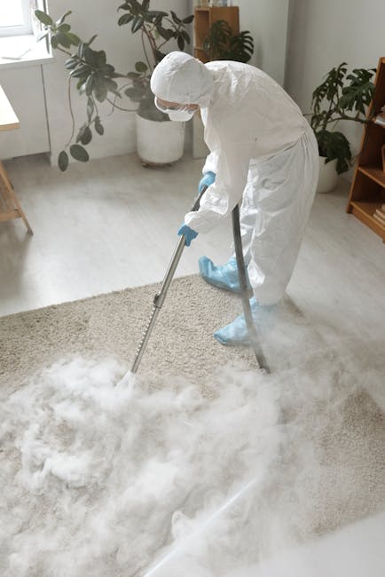 A woman with curly, shoulder-length hair, dressed in a beige jacket, dark jeans, and white sneakers, is performing surface cleaning using a yellow vacuum cleaner with a hose attachment on a patterned,